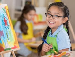 Little girl smiling and painting a colorful canvas